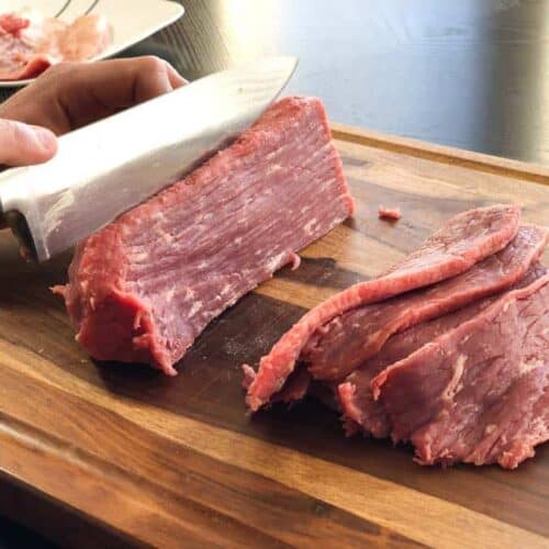 Eye of round beef roast being sliced in cutting board