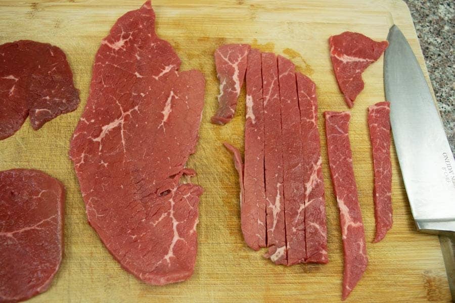 Beef top round sliced thin on cutting board with knife