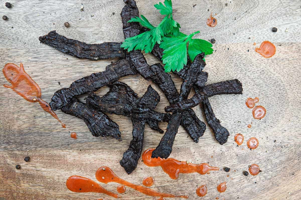 Beef jerky on cutting board with hot sauce