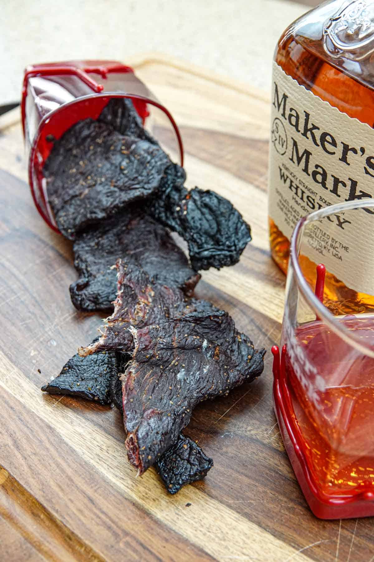 Beef jerky in bourbon glass with bottle of makers mark bourbon