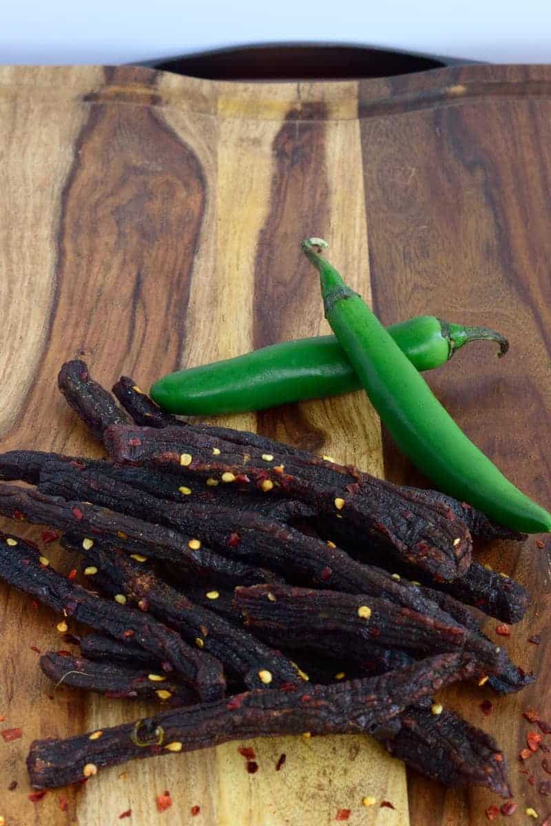 Spicy beef jerky on cutting board with green serrano peppers