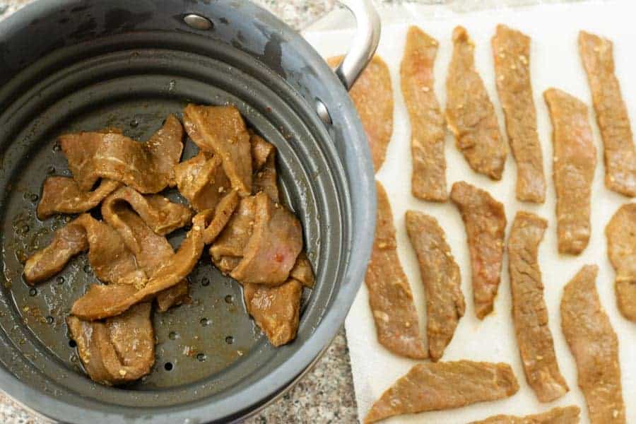 Patting dry jerky strips on paper towels after strained in colander