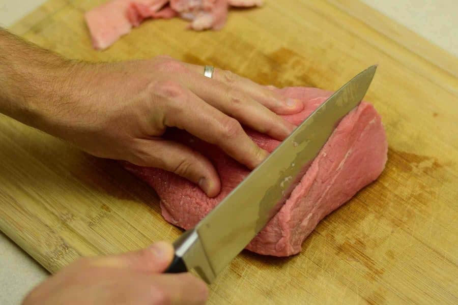 Slicing meat for jerky on cutting board with sharp knife
