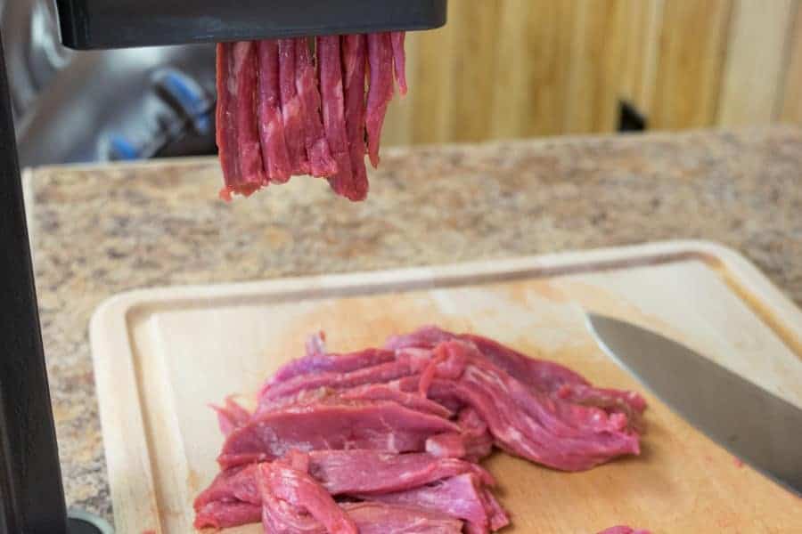 Beef Jerky slicer slicing beef for jerky onto a cutting board with knife