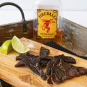 Fireball whisky bottle behind beef jerky on cutting board with two lime wedges