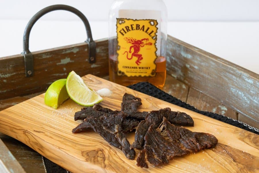 Fireball whisky bottle behind beef jerky on cutting board with two lime wedges