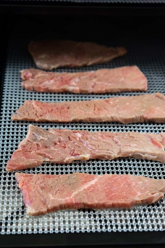 Beef jerky strips on dehydrator tray ready to dry