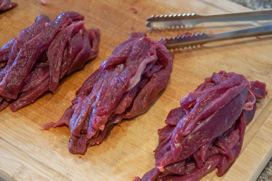Venison sliced for jerky on cutting board with tongs