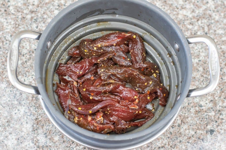 Deer jerky strained in colander before dehydrating