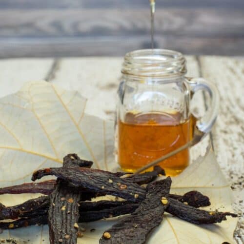 Peppered honey deer jerky on a leaf with a jar of honey with wood background