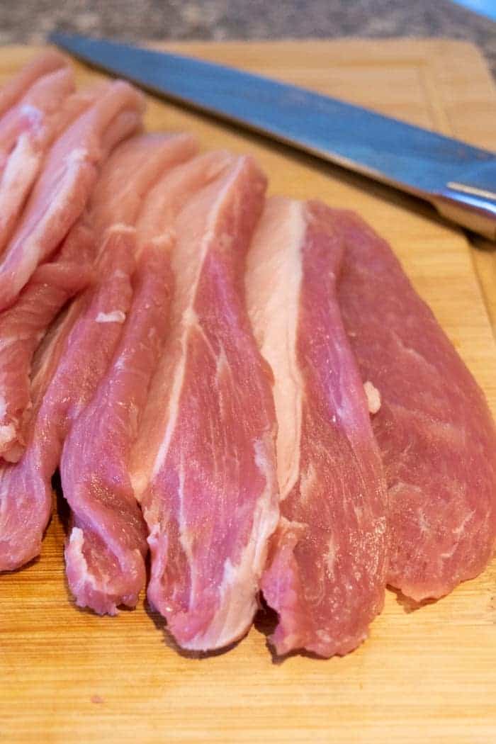 Pork loin sliced for jerky on the cutting board with a knife