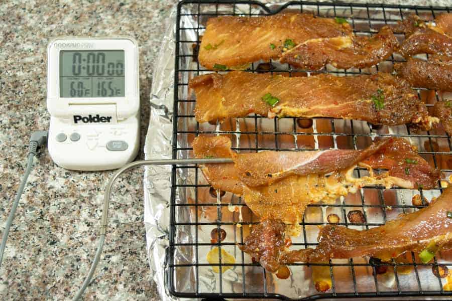 Korean BBQ pork jerky on an oven tray with a thermometer