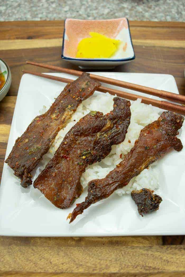 Korean BBQ pork jerky strips sitting on rice with chopsticks