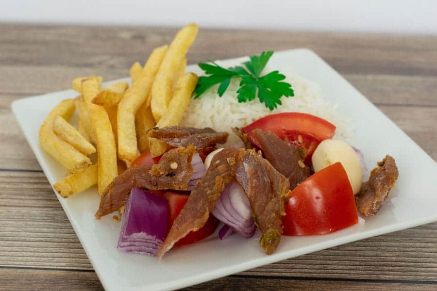 Peruvian jerky on plate with tomatoes, rice and french fries