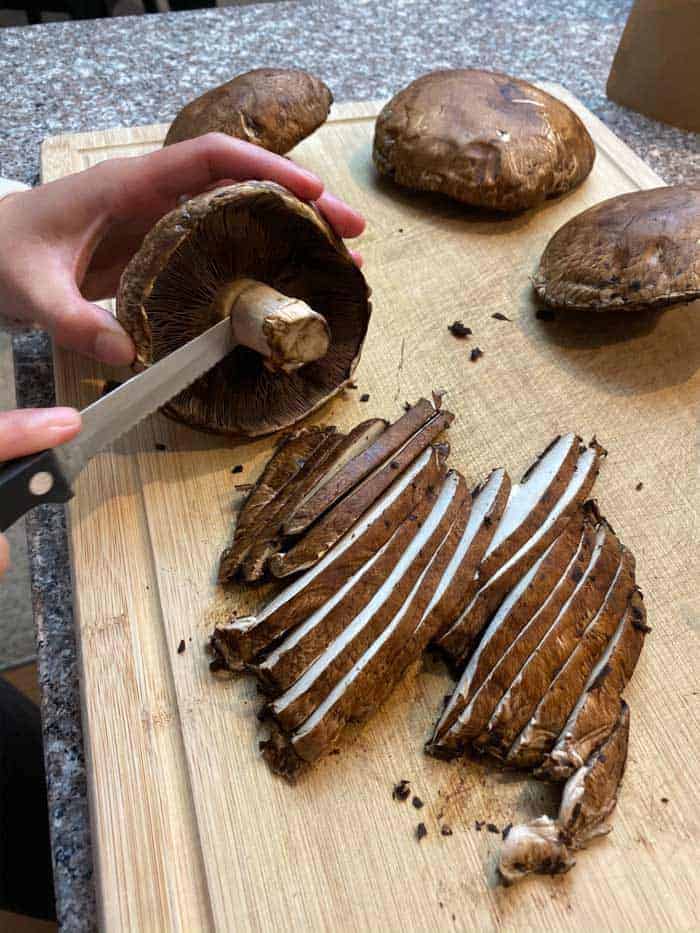 Hands slicing Portobello mushrooms in even strips on cutting board