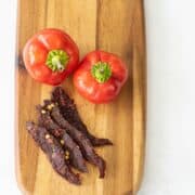 Cherry bomb beef jerky on cutting board with peppers