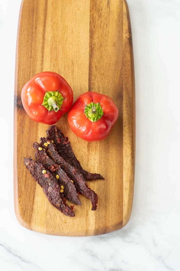 Cherry bomb beef jerky on cutting board with peppers