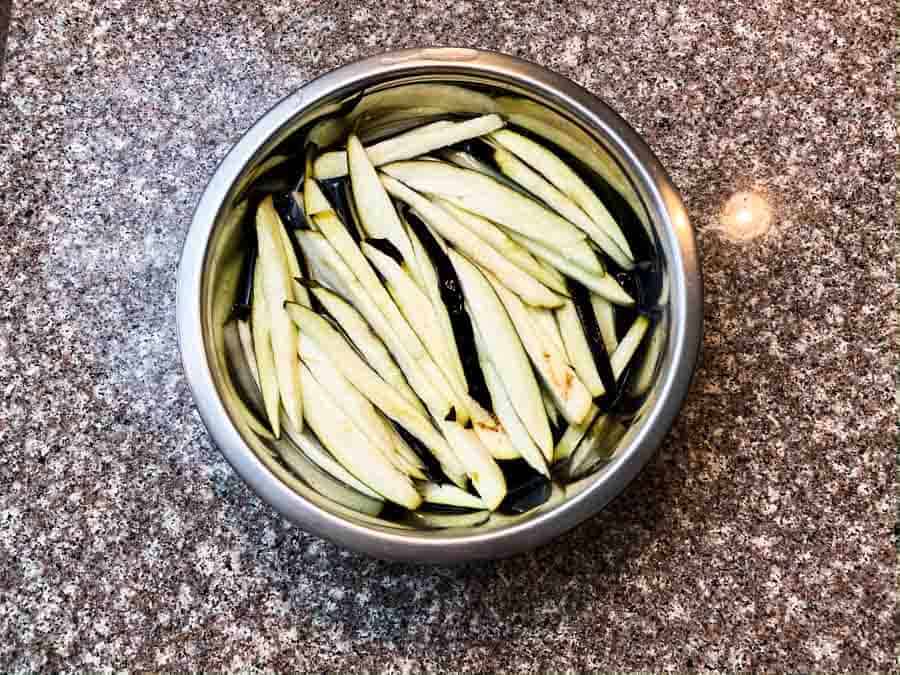 eggplant slices soaking in salt water in silver bowl