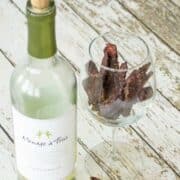 Bottle of white wine on wooden table next to a wine glass with beef jerky inside