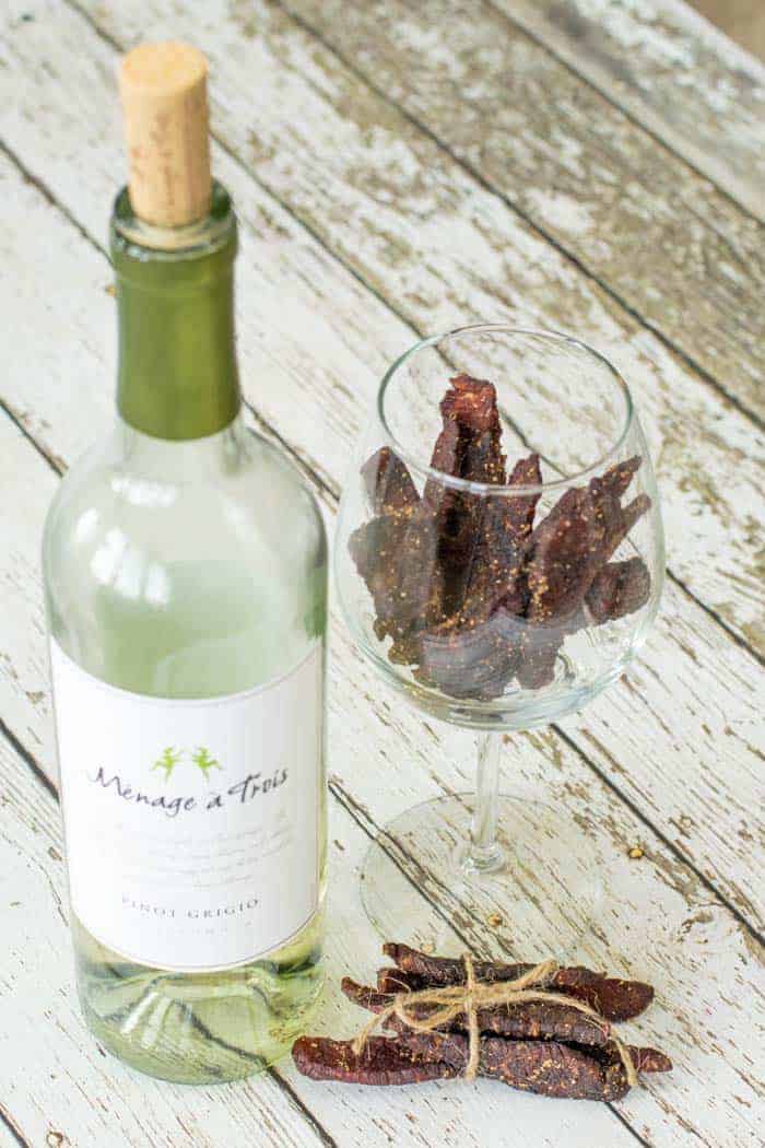 Bottle of white wine on wooden table next to a wine glass with beef jerky inside