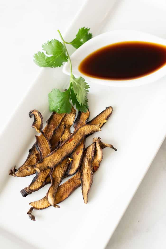 Mushroom jerky on white plate with green garnish and soy sauce in small dish