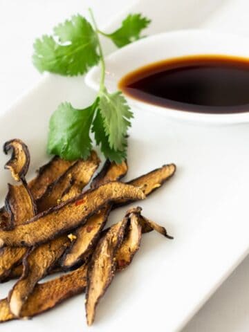 Mushroom Jerky on white plate with soy sauce on side