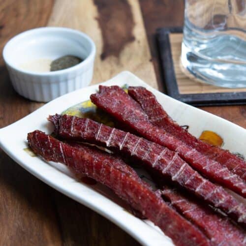 Beef jerky on plate with spices and glass of water