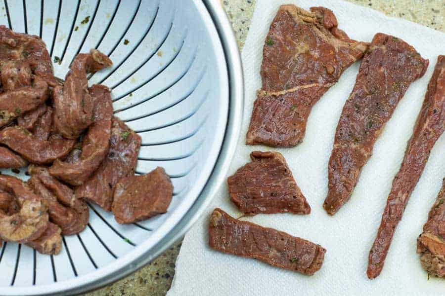 Marinated jerky strips in colander and on paper towels