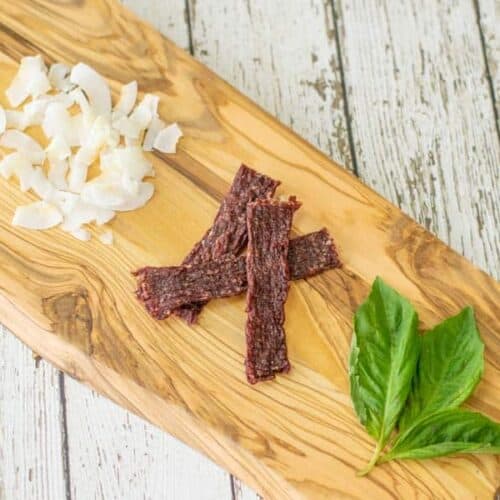 coconut ground beef jerky on cutting board with coconut shavings and basil