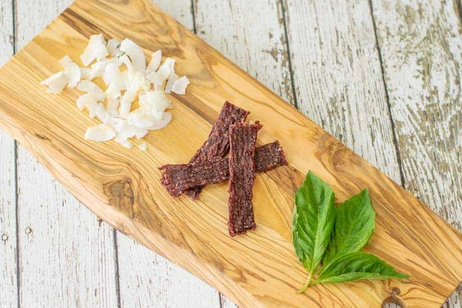 coconut ground beef jerky on cutting board with coconut shavings and basil