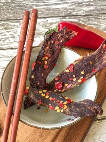Venison jerky in bowl with chop sticks on cutting board