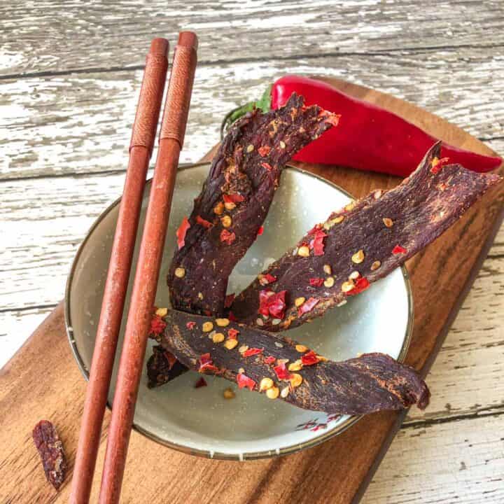Venison jerky in bowl with chop sticks on cutting board