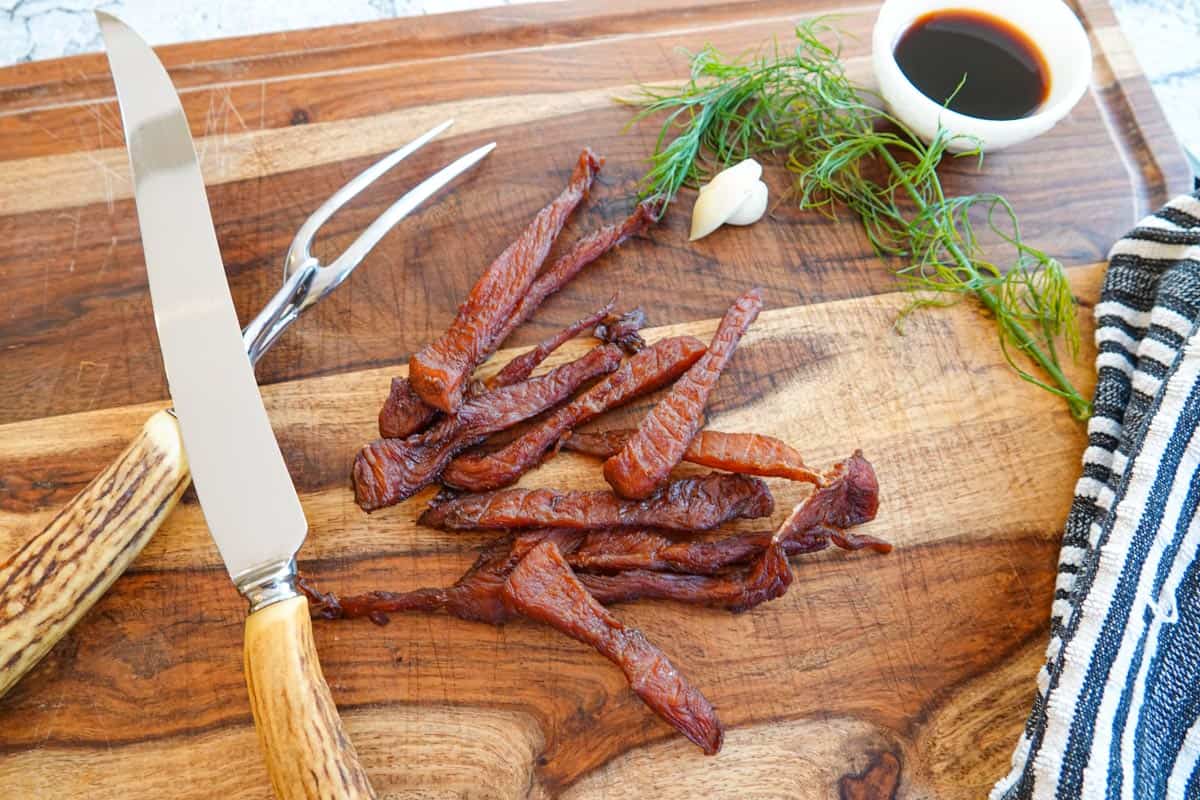 Turkey jerky on cutting board with carving knife and dish of soy sauce