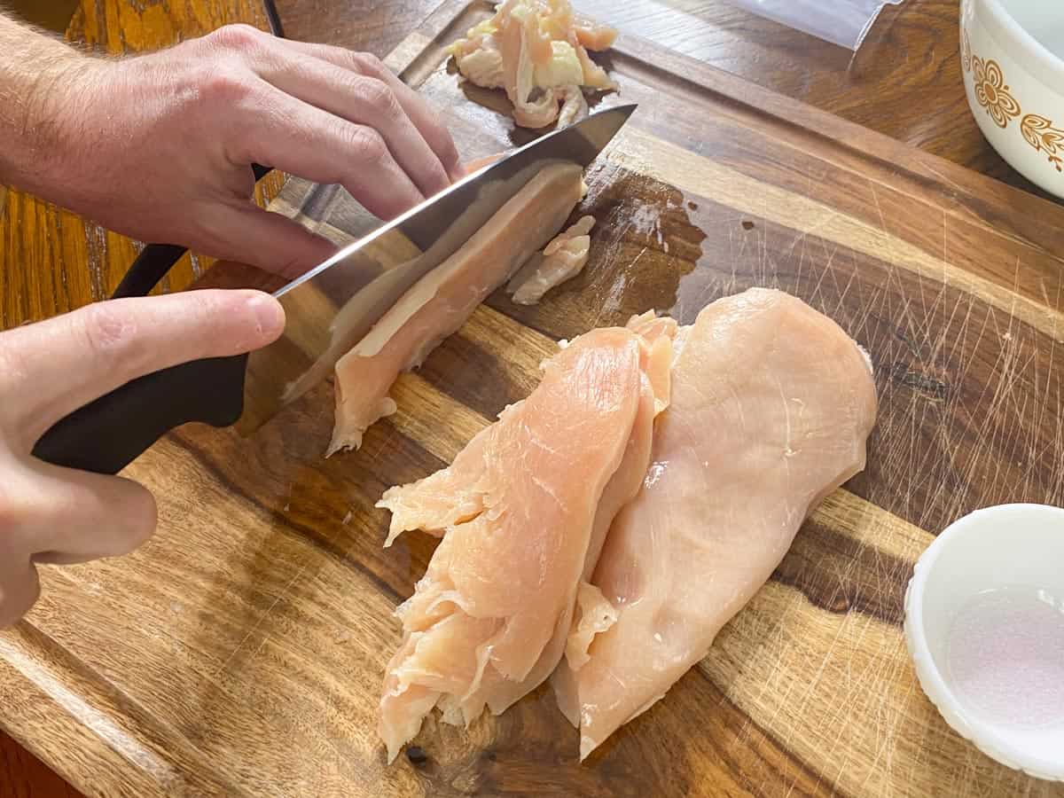 chicken breast being sliced into thin strips on cutting board for making chicken jerky.