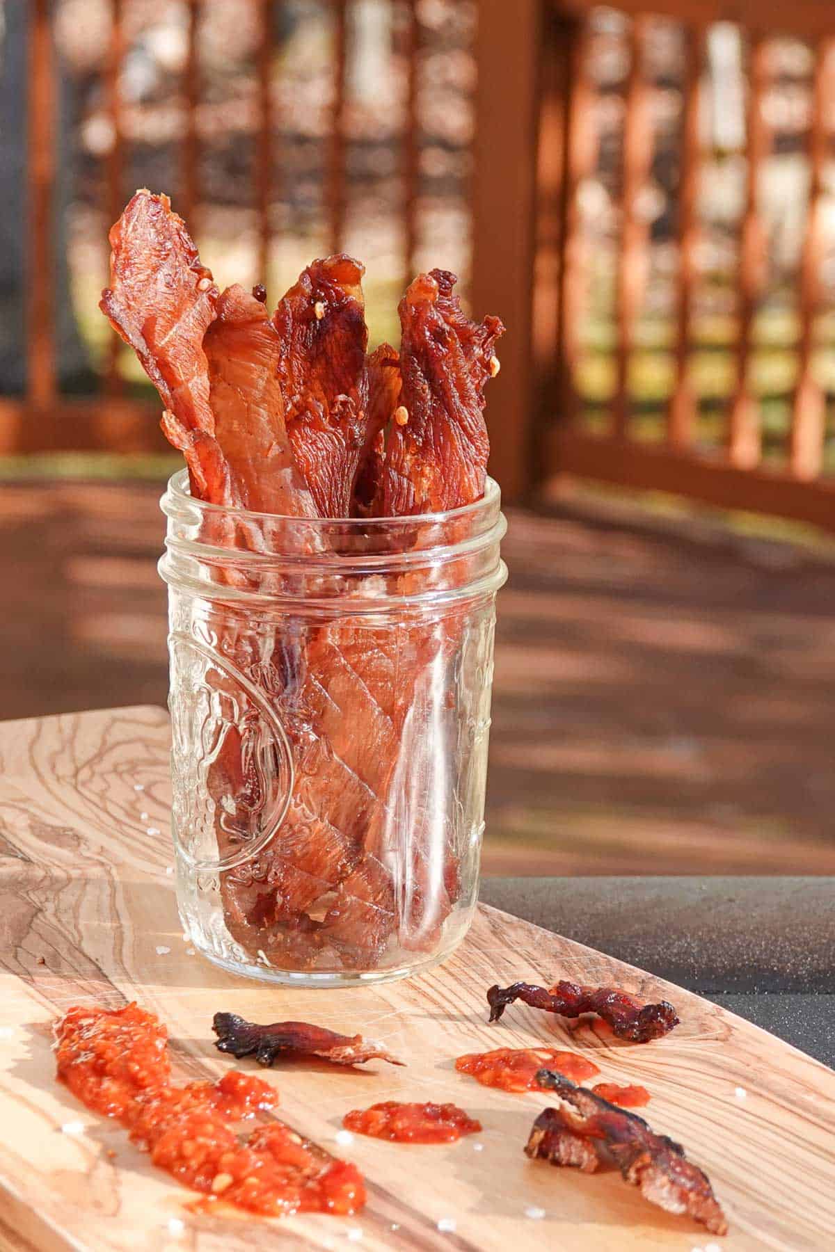 chicken jerky in a jar on cutting board with sauce on cutting board