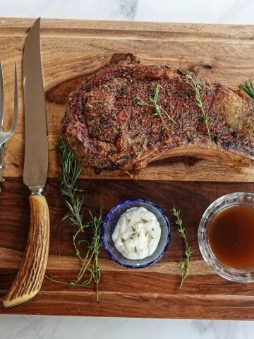 rib roast on cutting board with knife, fork, au jus, and horseradish sauce