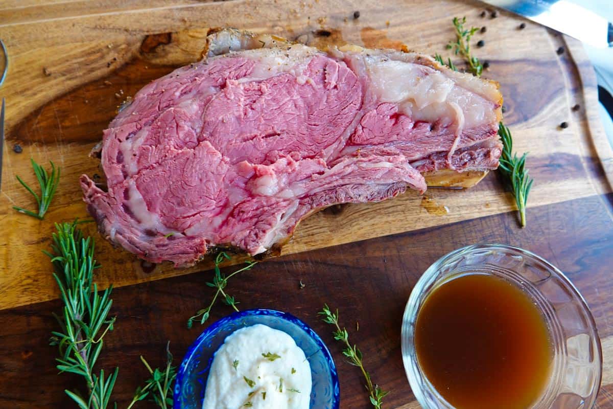 Prime rib roast sliced on cutting board with horseradish and au jus.