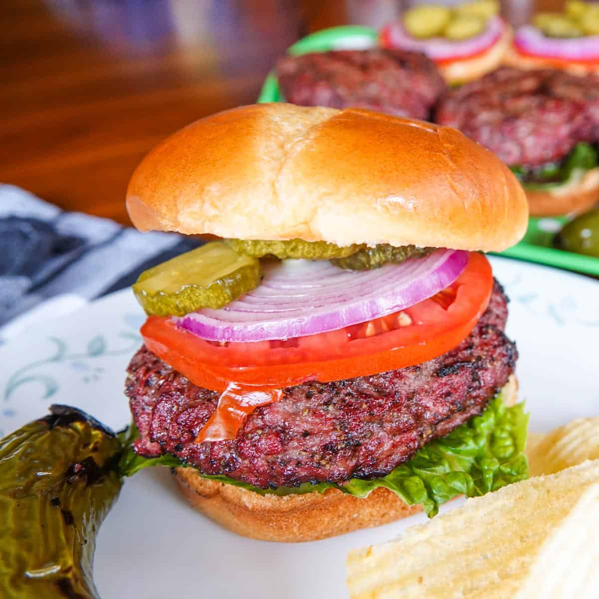 Hamburger with tomato, pickles, onions on plate with burgers in background