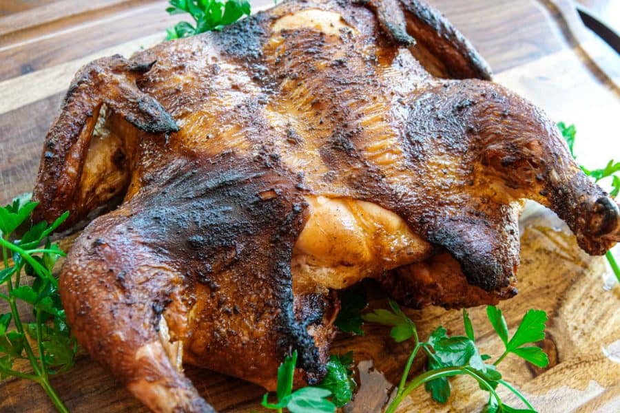 whole smoked chicken on cutting board with green garnish