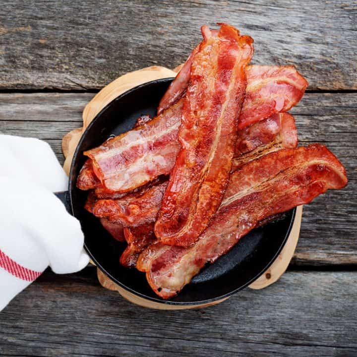 Bacon in frying pan on wood background