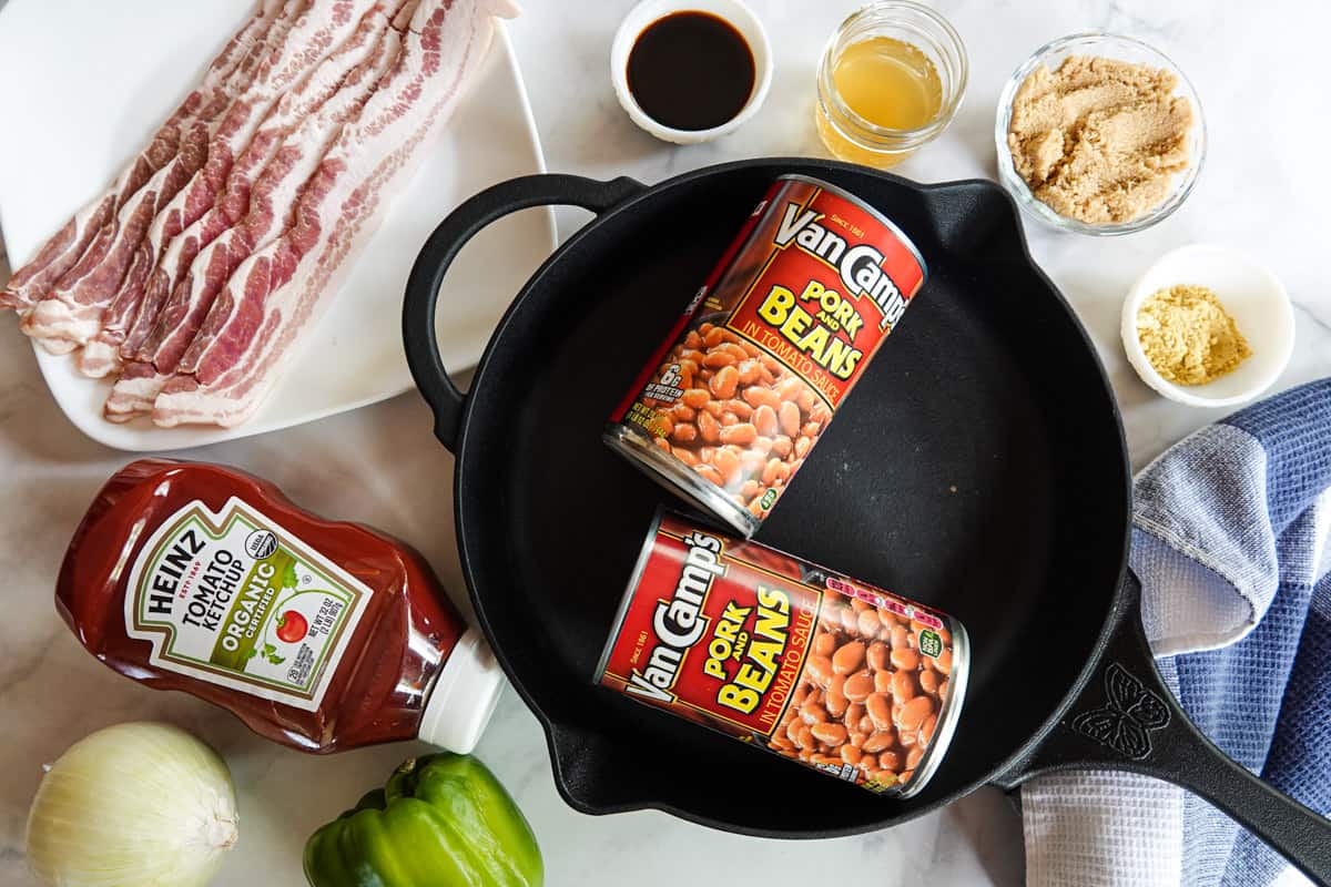 canned beans inside cast iron pan with bacon and other ingredients around