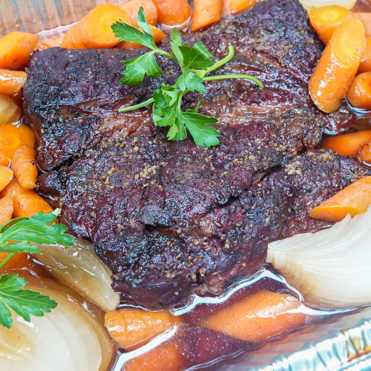 chuck roast in pan with beef broth, carrots, and onions garnished with parsley