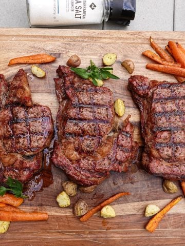 Three smoked steaks on cutting board with carrots and potatoes