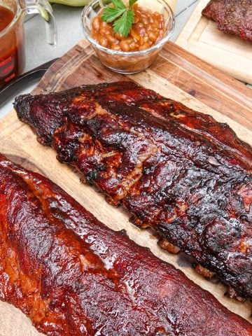 Two racks of ribs on cutting board with baked beans