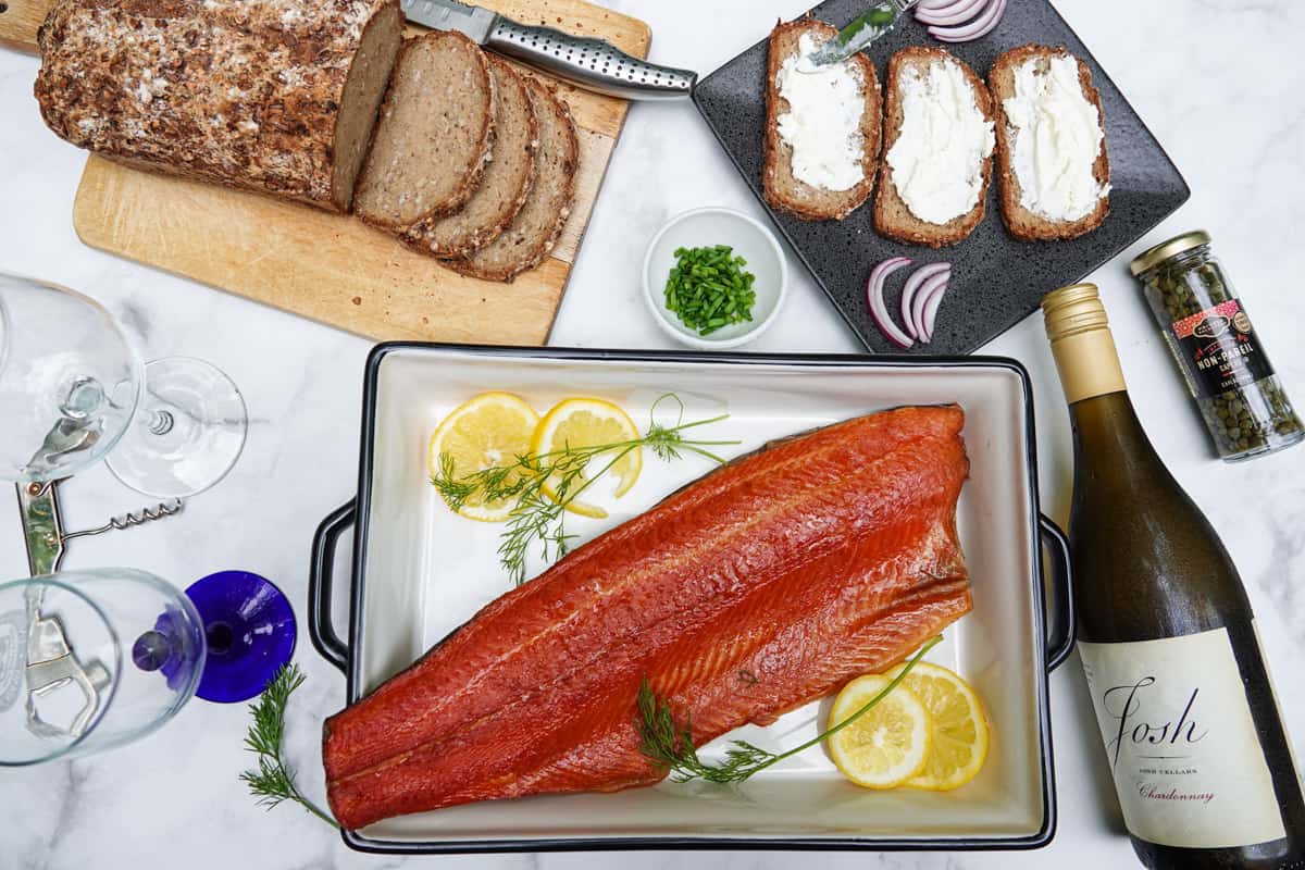 Smoked trout fillet in dish with bottle of wine, bread, toast, and seasonings