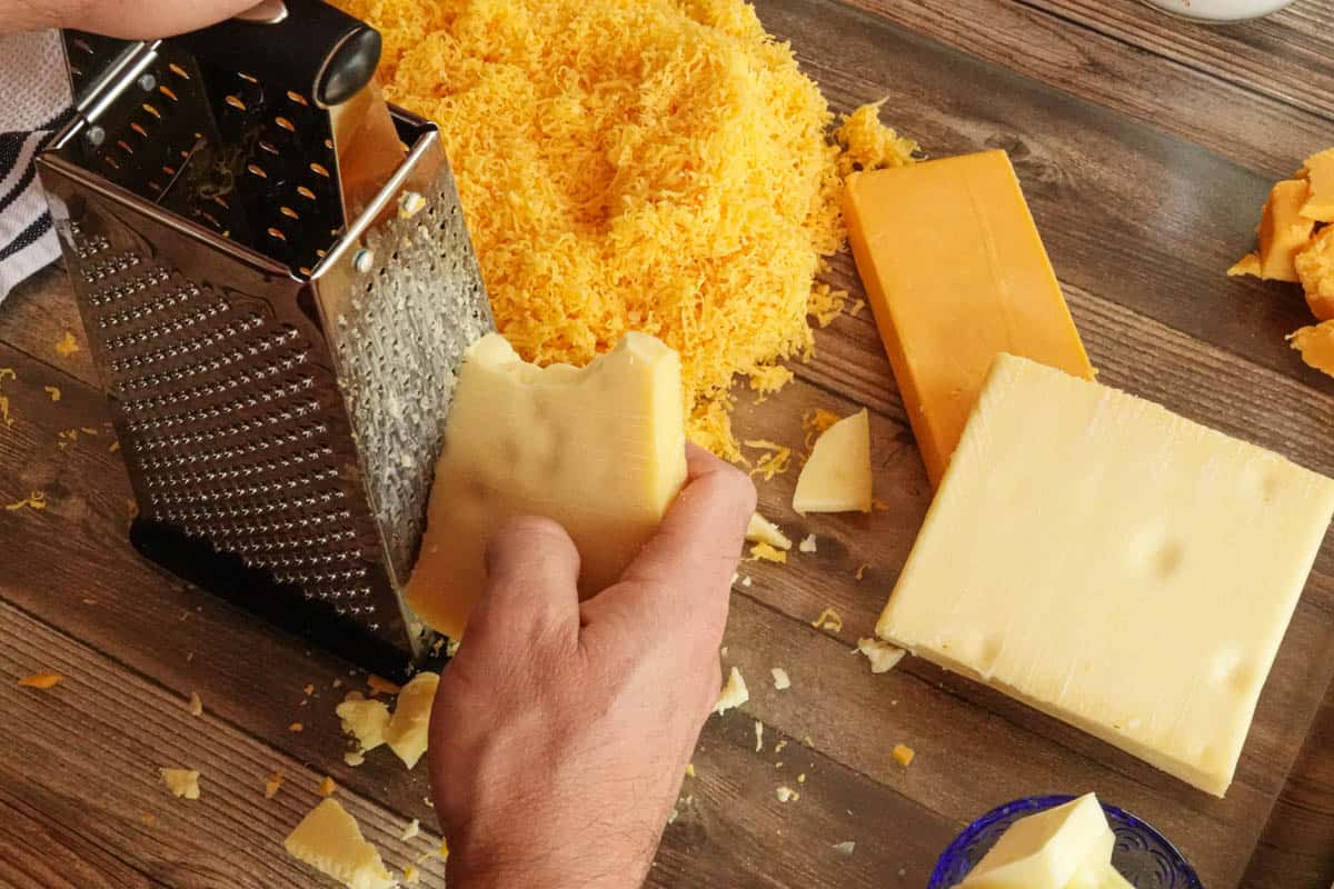Cheese being grated by hand on cutting board
