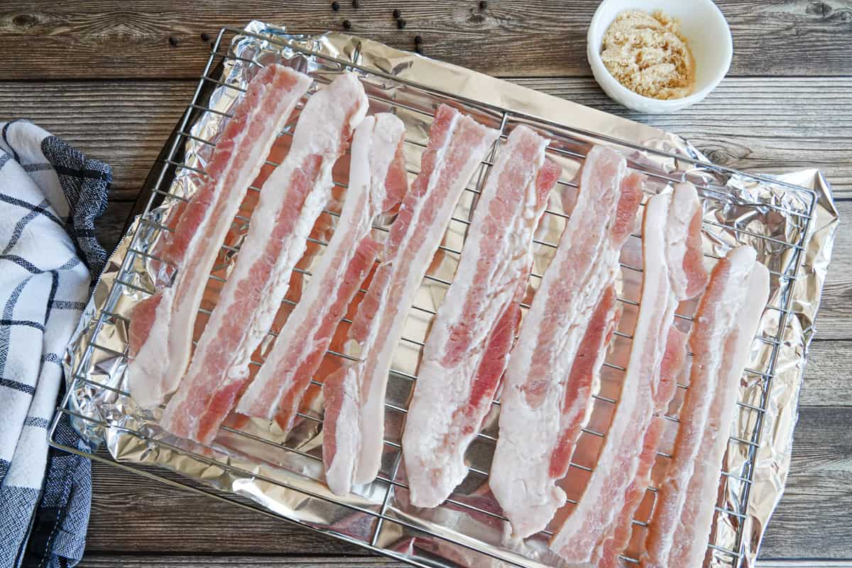 Bacon on oven tray with towel and dish with brown sugar in background
