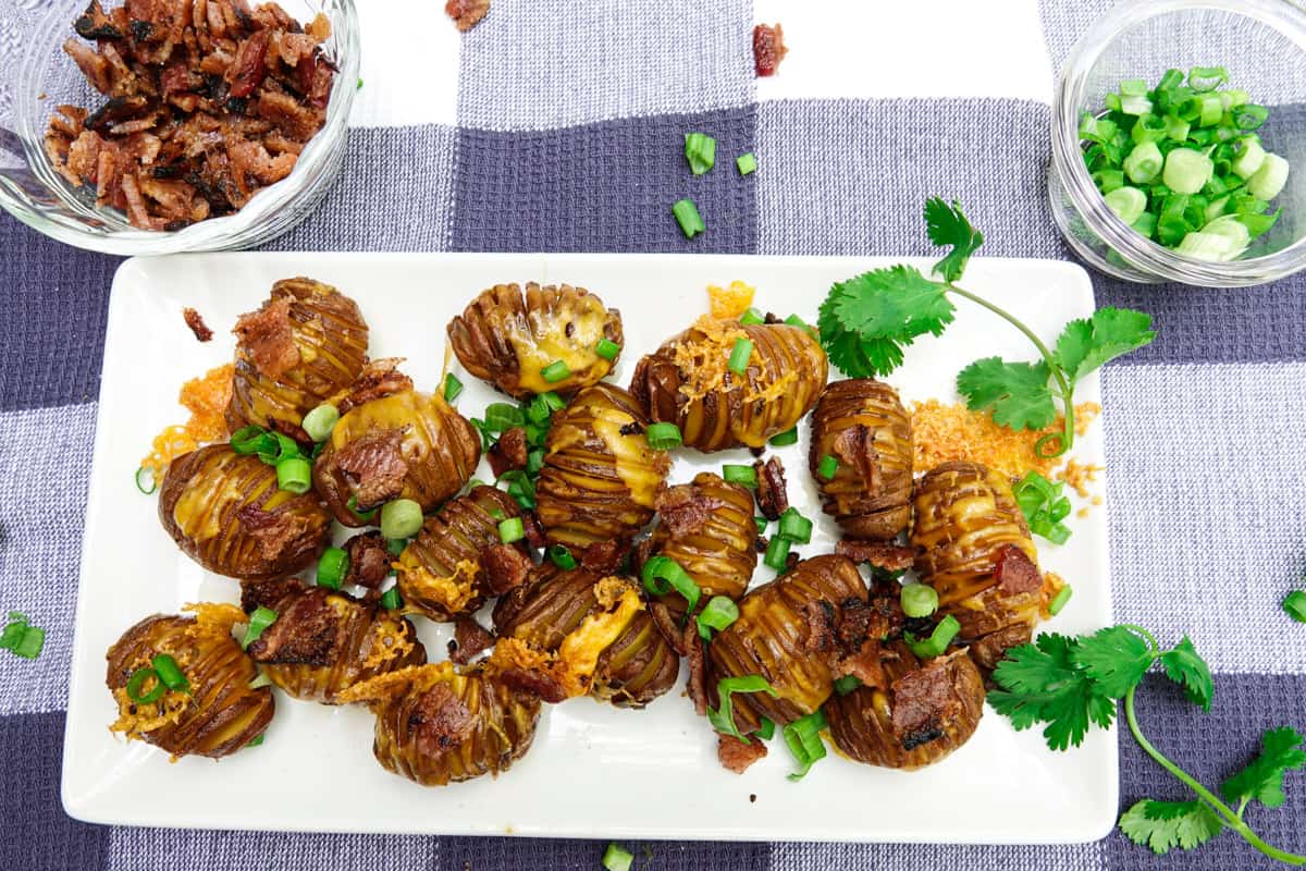 Hasselback potatoes plated on white plate with cup of bacon and green onions