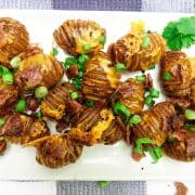 Hasselback potatoes on white dish with bacon and green onions on top