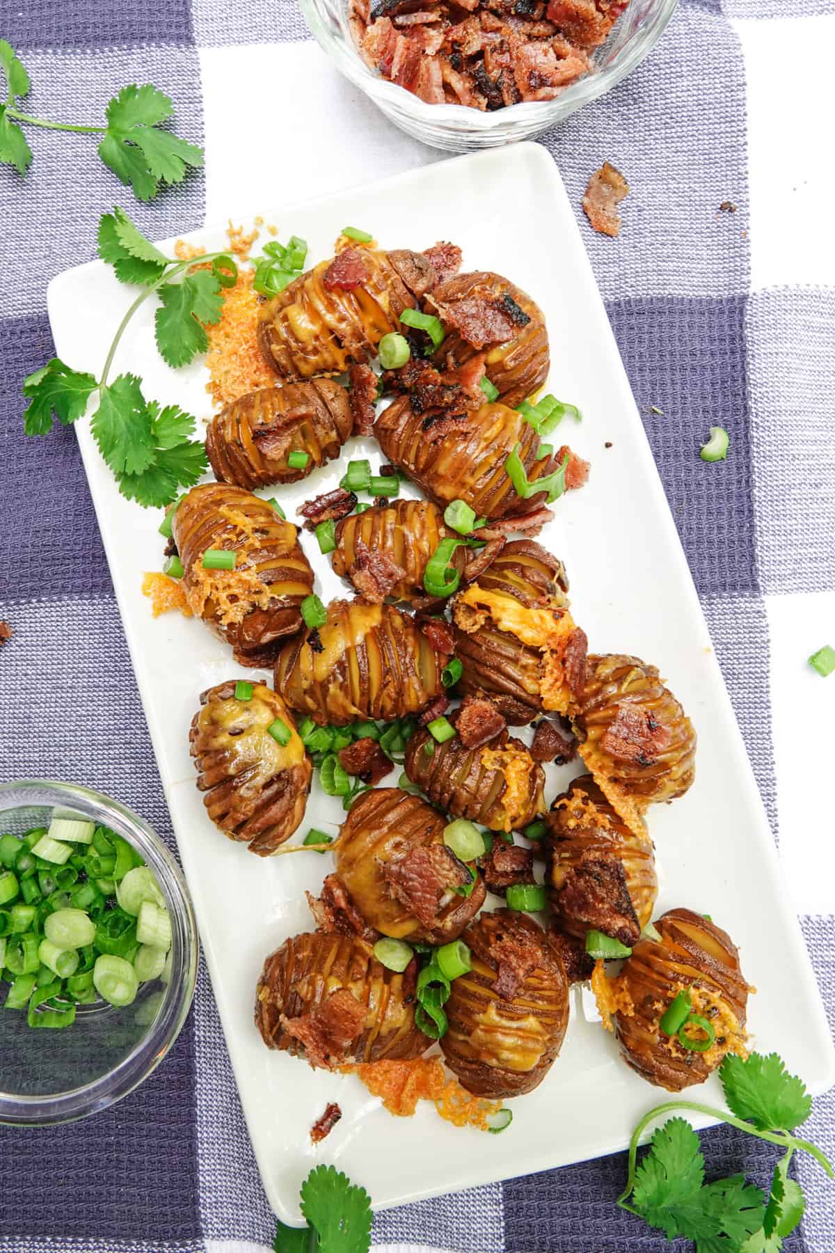 hasselback potatoes on white serving dish with green onions sprinkled on top